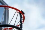 Close-up of a basketball hoop with a red rim, white net, and black support structure against a cloudy blue sky.